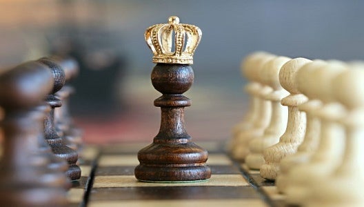 pawn chess piece with a crown on top, sitting on a chess board